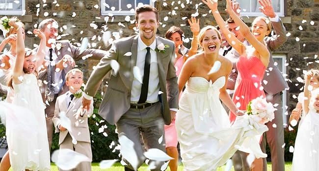 Wedding party throwing ivory white rose petals in the air, bride and groom smiling