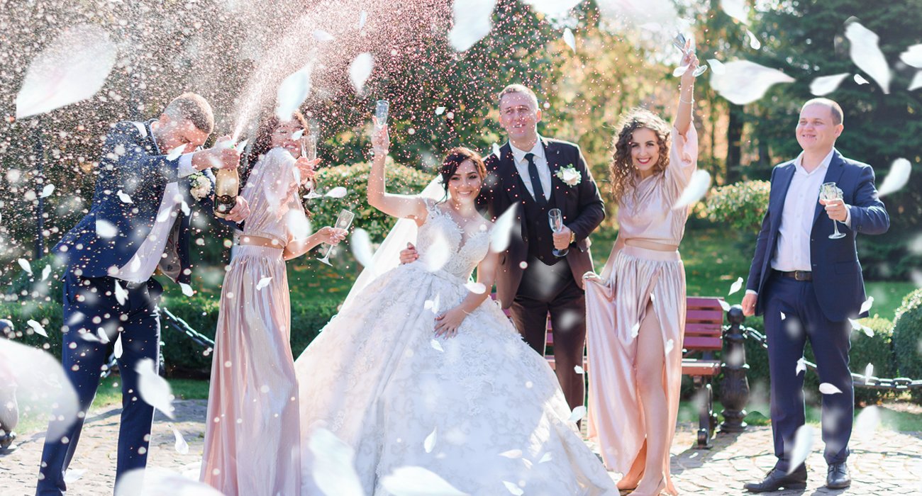Wedding party celebrating with champagne and falling rose petals outdoors