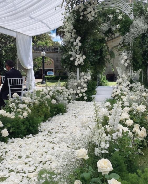 Wedding aisle decorated with white rose petals and flowers, leading to an archway.