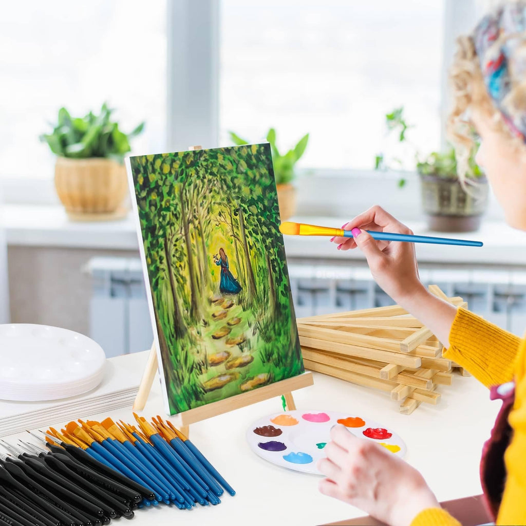 Woman painting a forest scene on canvas with brushes and palette, surrounded by art supplies
