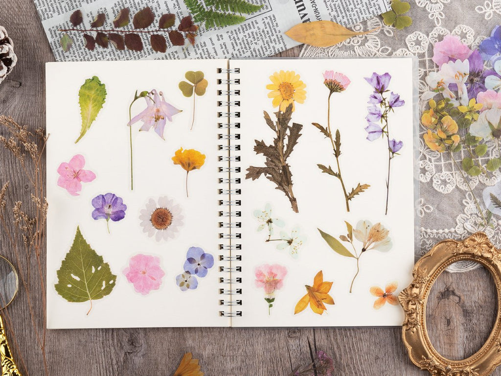 Assortment of pre-cut botanical PET stickers featuring flowers and leaves arranged on an open notebook page.