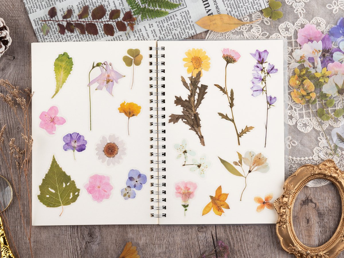 Assortment of pre-cut botanical PET stickers featuring flowers and leaves arranged on an open notebook page.