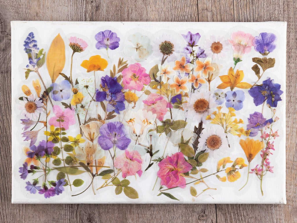 Flat lay of a canvas covered in pre-cut botanical PET stickers featuring various pressed flowers and leaves in vibrant colors.