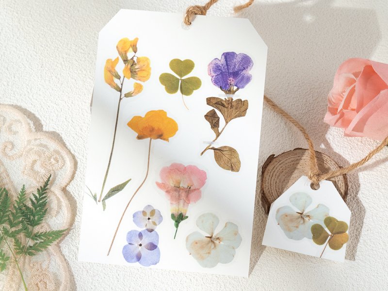 Sheet of pre-cut botanical PET stickers featuring pressed flowers and leaves, with a smaller tag showing two stickers.