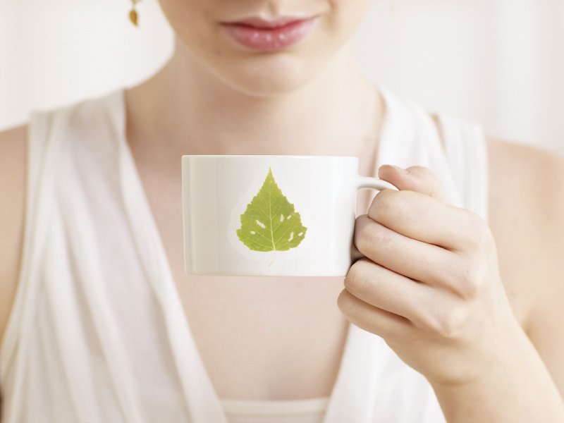 Woman holding a white mug with a green leaf sticker on it, close-up shot