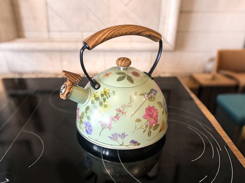 Light green floral patterned stovetop kettle with a wood-grain handle, set on a black electric stovetop.