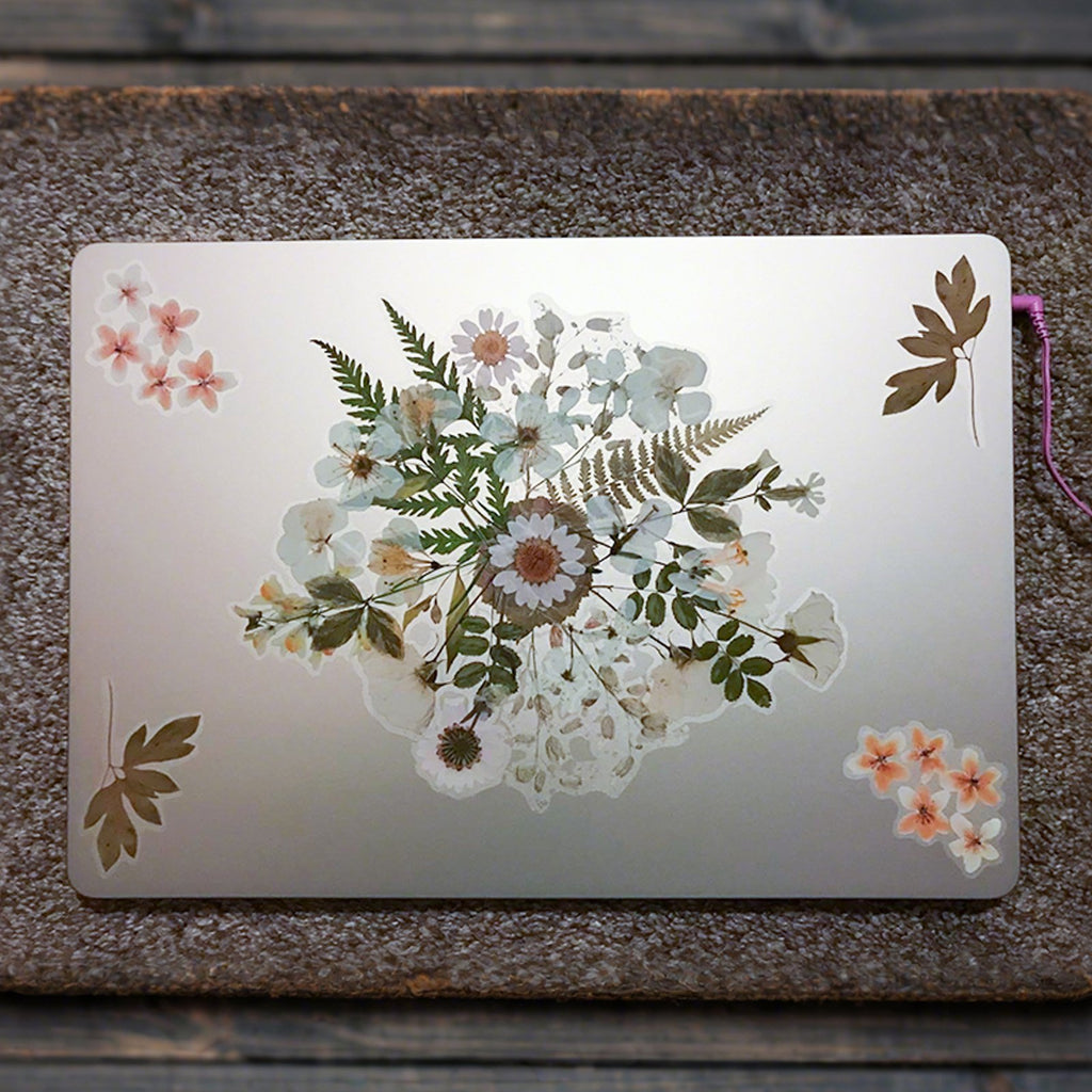 Botanical PET stickers arranged on a silver laptop lid, featuring floral and leaf designs.