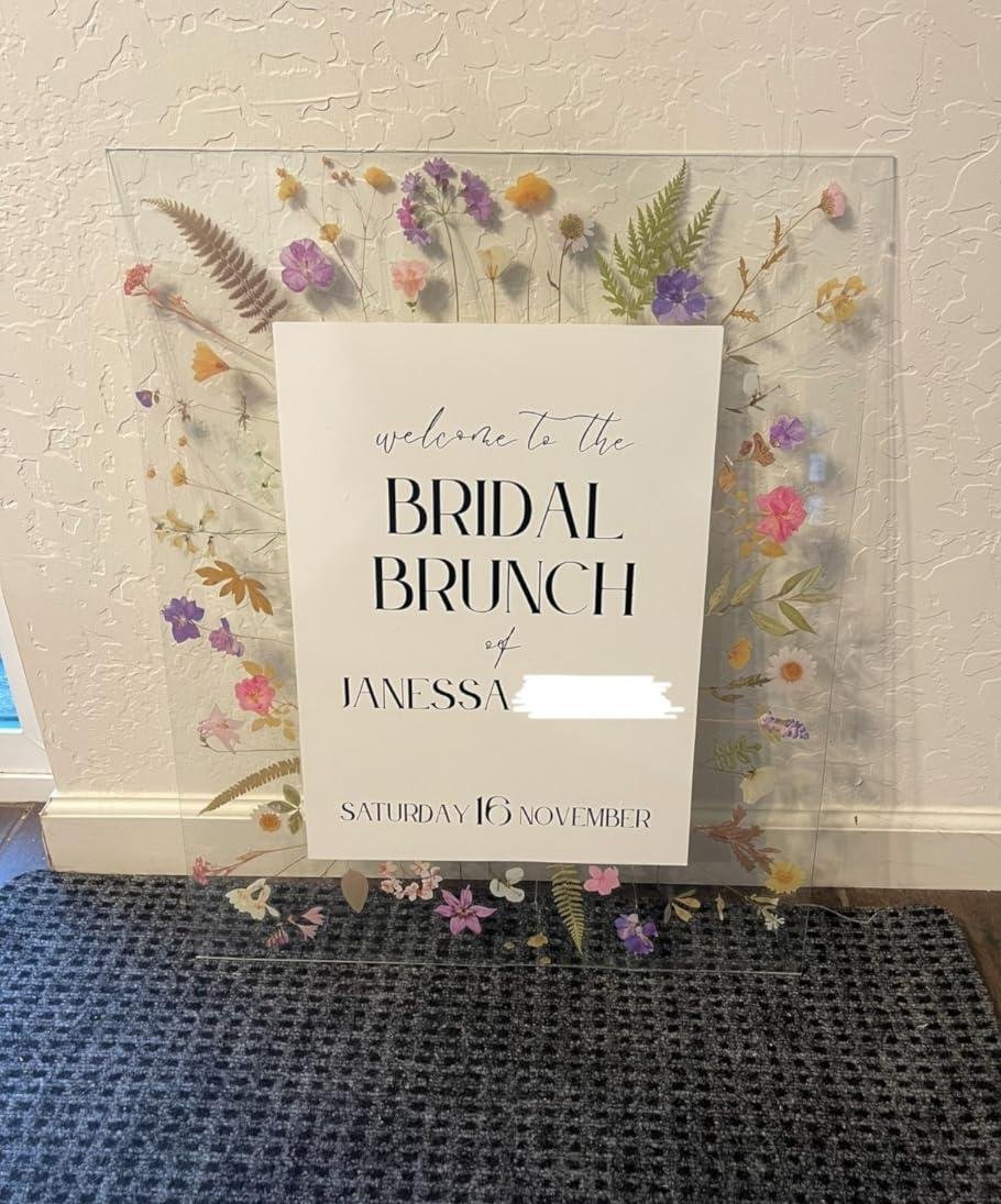 Clear acrylic sign with dried flowers and text for a bridal brunch event.