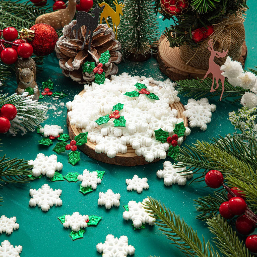 Christmas craft assortment of white snowflakes and green holly berries scattered on a teal surface with pine branches and festive decorations.