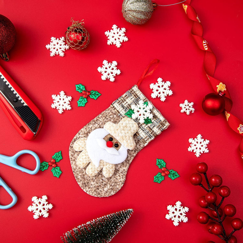 Christmas craft assortment including a Santa stocking, snowflakes, holly berries, ornaments, ribbon, scissors, and a craft knife on a red background.