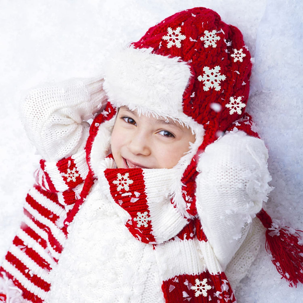 Child in red snowflake hat and striped scarf lying in snow, smiling