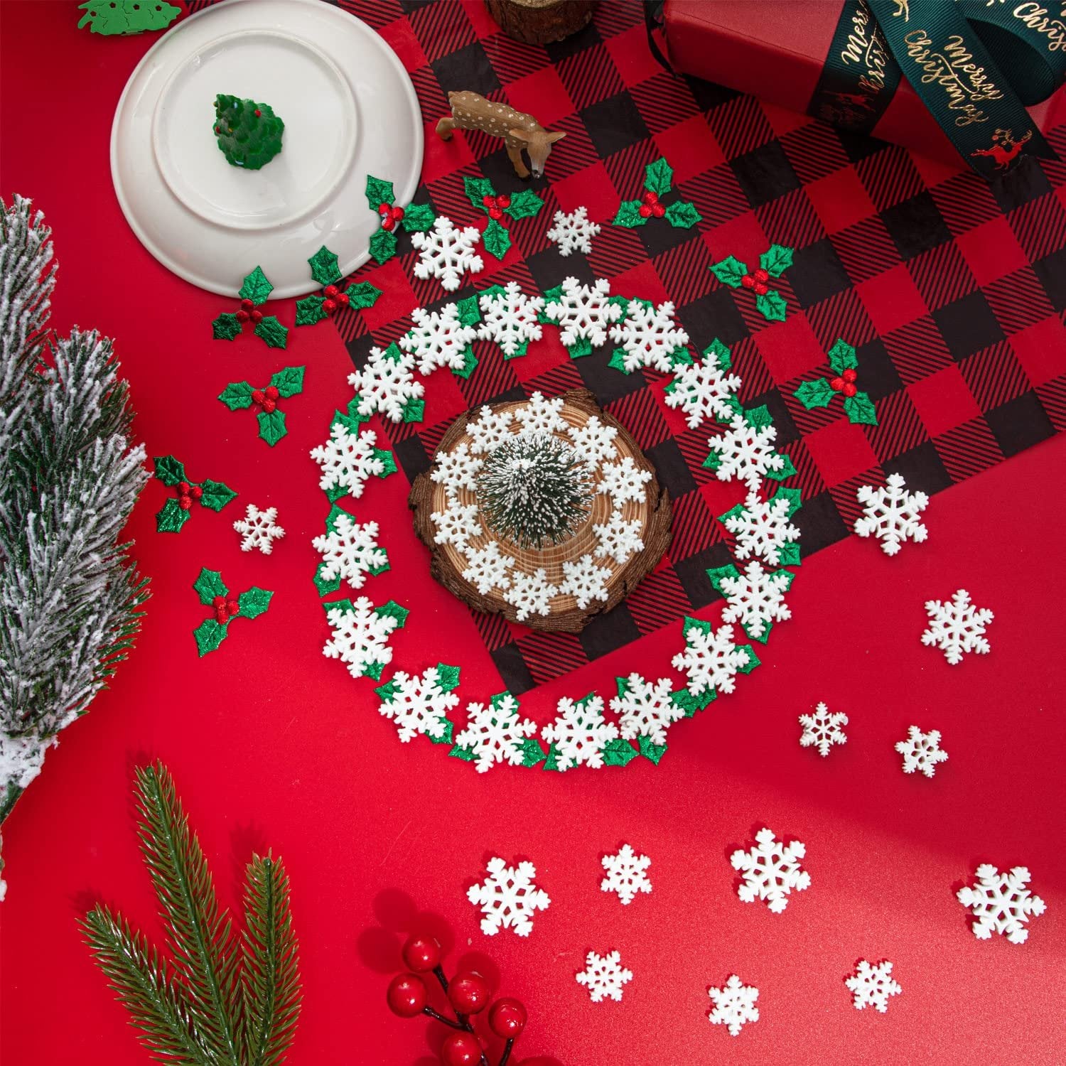 Christmas craft assortment with white snowflakes and green holly berries arranged on a red background.