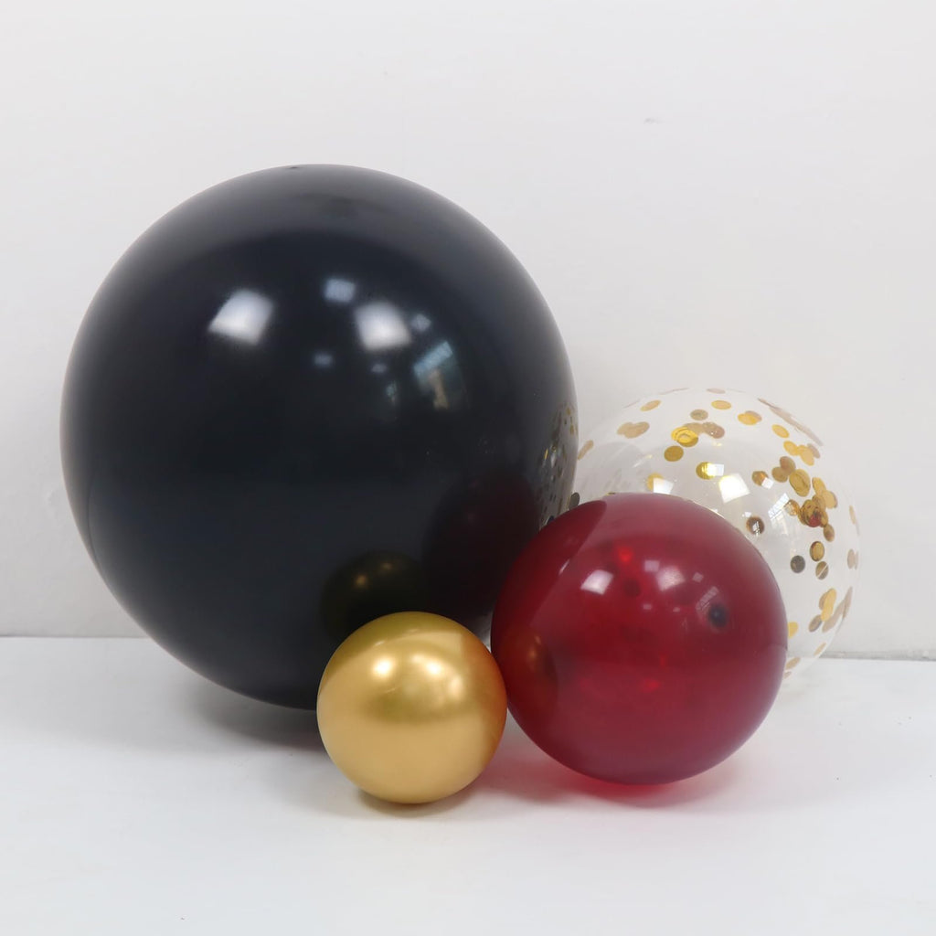Burgundy, black, gold, and confetti balloons arranged on a white surface against a white background.