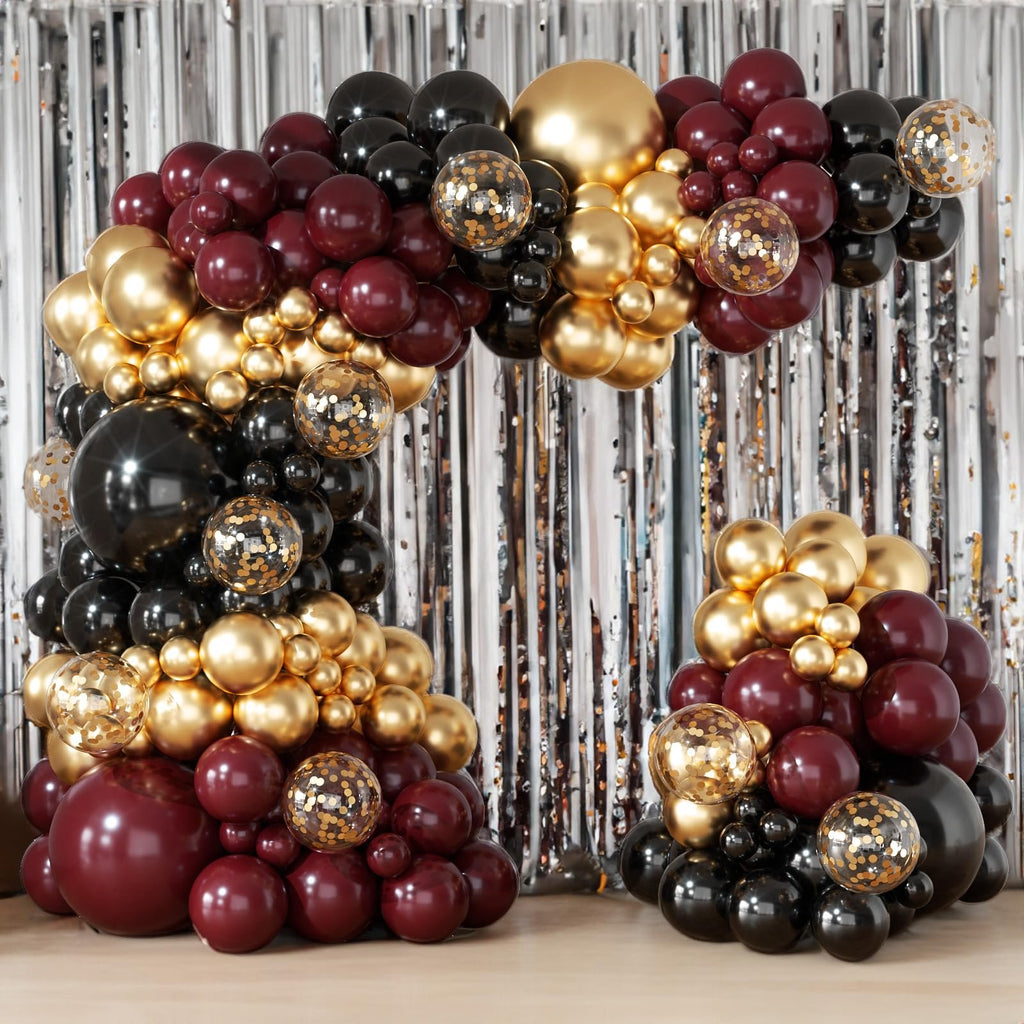 Burgundy, black, and gold balloon arch garland with confetti balloons against a silver tinsel backdrop.