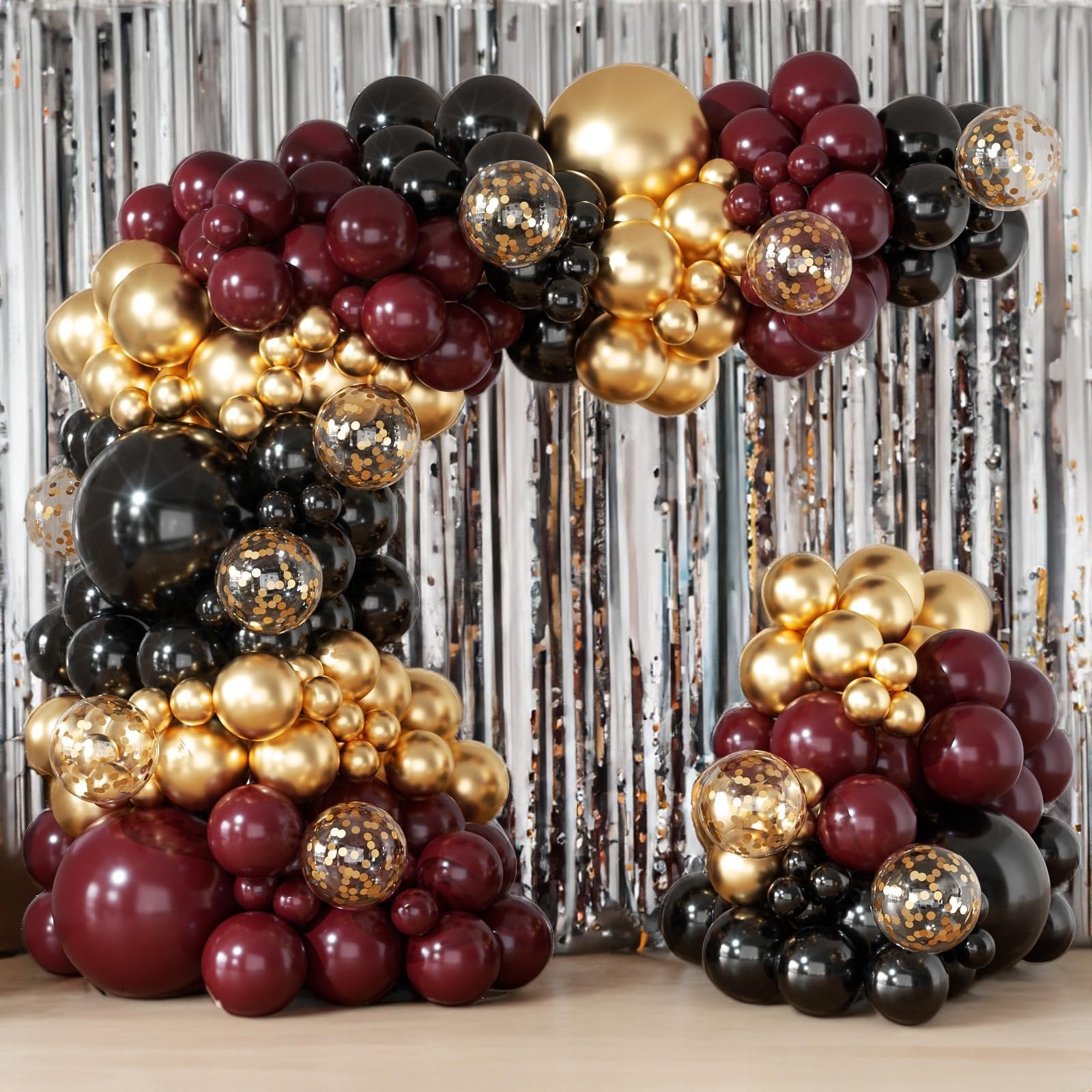 Burgundy, black, and gold balloon arch garland with confetti balloons against a silver tinsel backdrop.