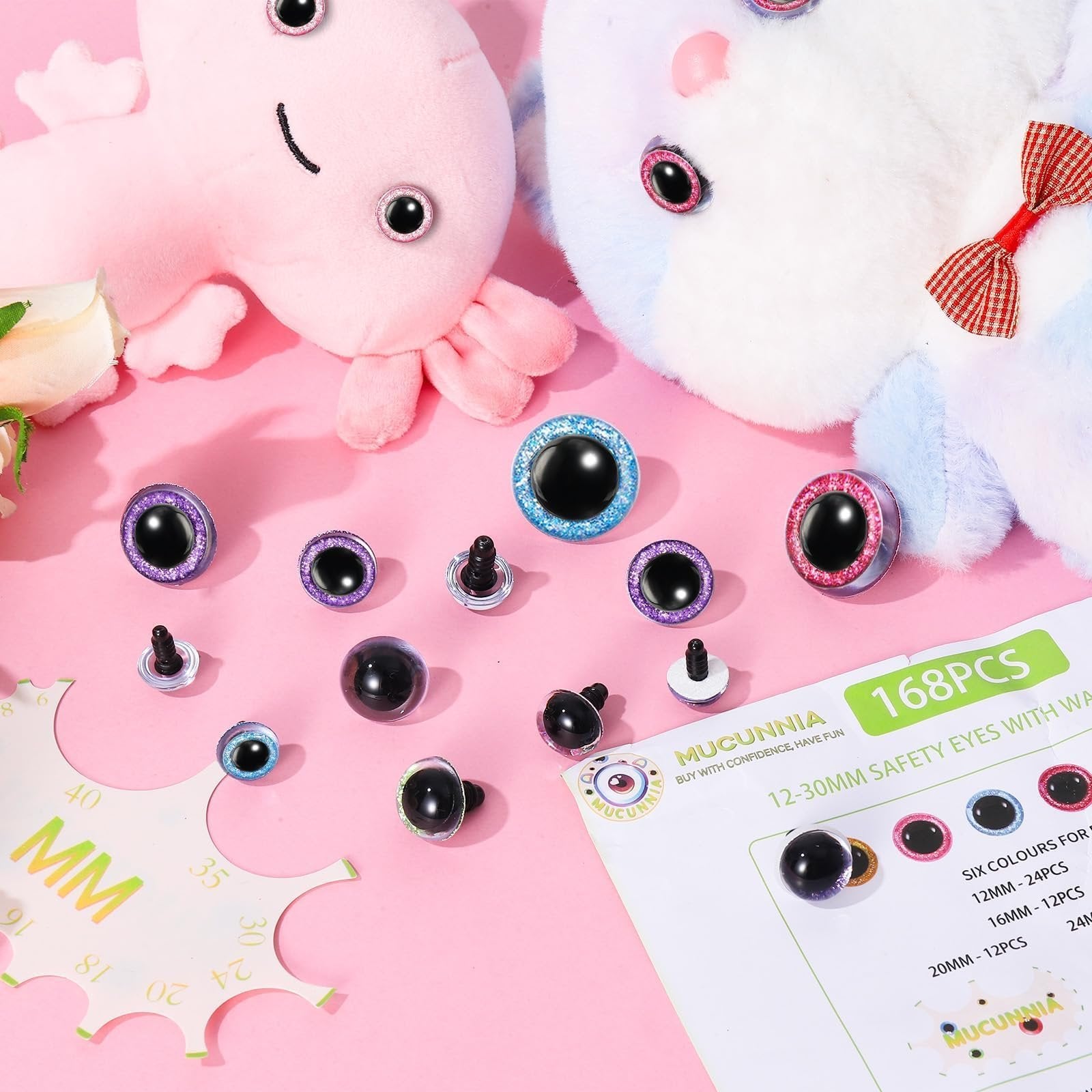 Assorted glitter safety eyes and washers scattered on a pink background with plush toys and a sizing tool.