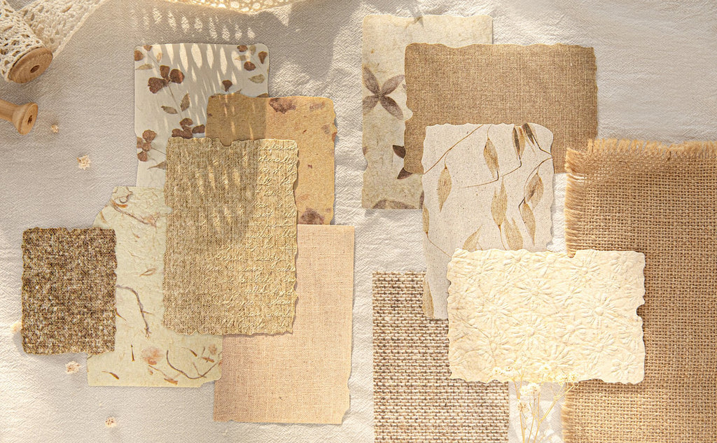 Assorted textured scrapbook papers with floral and leaf patterns, arranged on a linen-like surface with decorative elements.