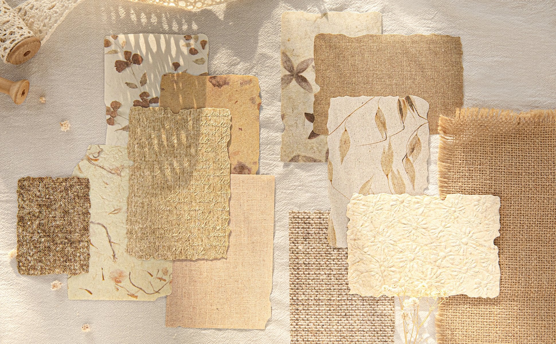 Assorted textured scrapbook papers with floral and leaf patterns, arranged on a linen-like surface with decorative elements.