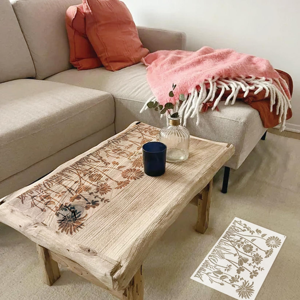 Flower stencil with wildflower designs on a rustic wooden table next to a couch with pillows and a blanket.