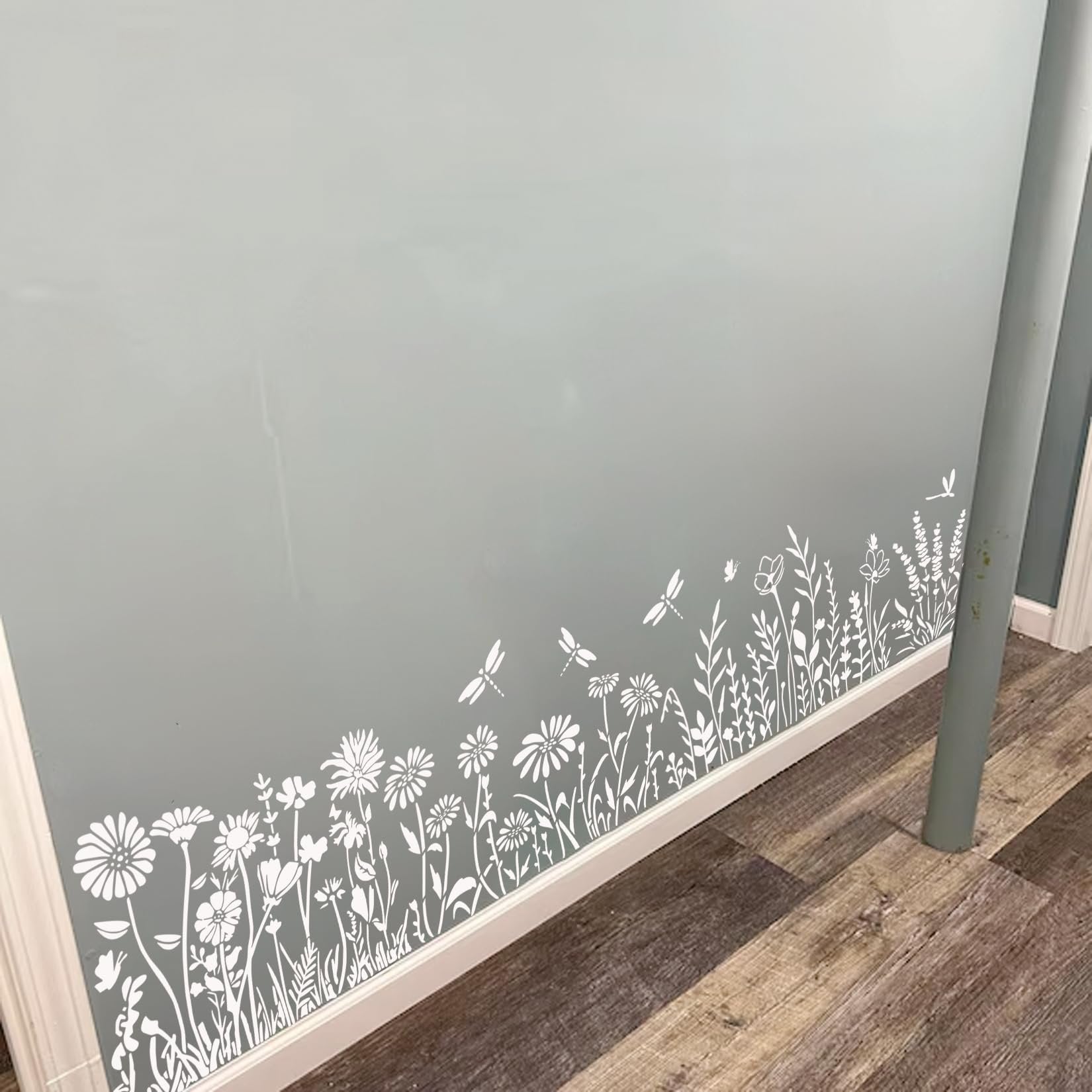 White wildflower and dragonfly stencils applied to a light blue wall near the floorboards.
