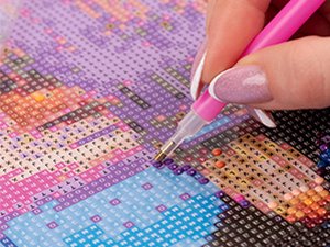 Close-up of a hand using a pink tool to place a diamond onto a 5D diamond painting canvas with a vase and flower design.