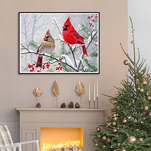 Diamond art painting of two cardinals on a snowy branch, framed and hanging above a fireplace with a Christmas tree nearby.