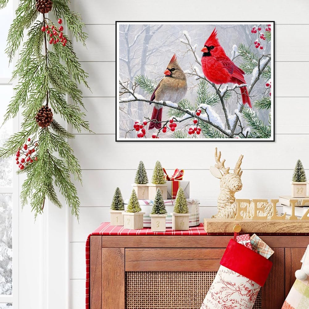 Diamond art painting of two cardinals perched on a snow-covered branch with red berries, framed and displayed above holiday decor.