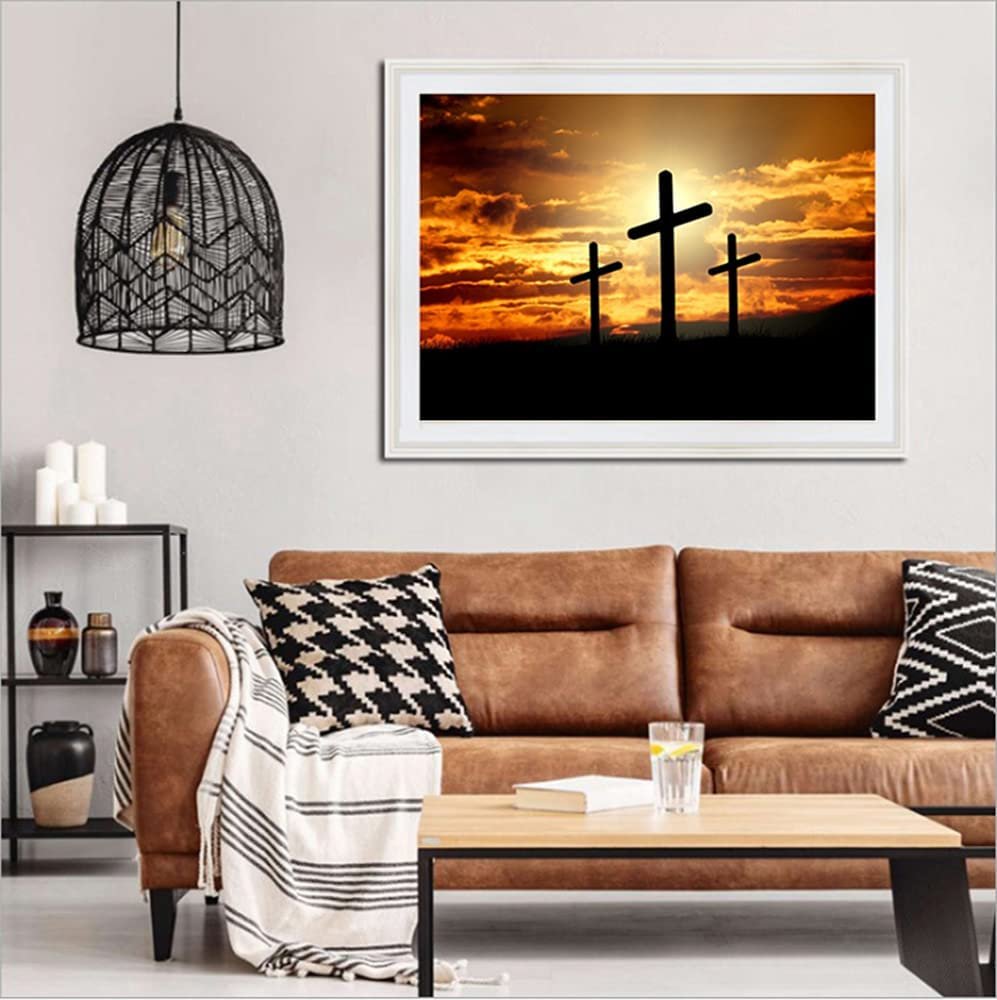 Framed diamond painting of three crosses silhouetted against a dramatic sunset sky, displayed above a sofa.