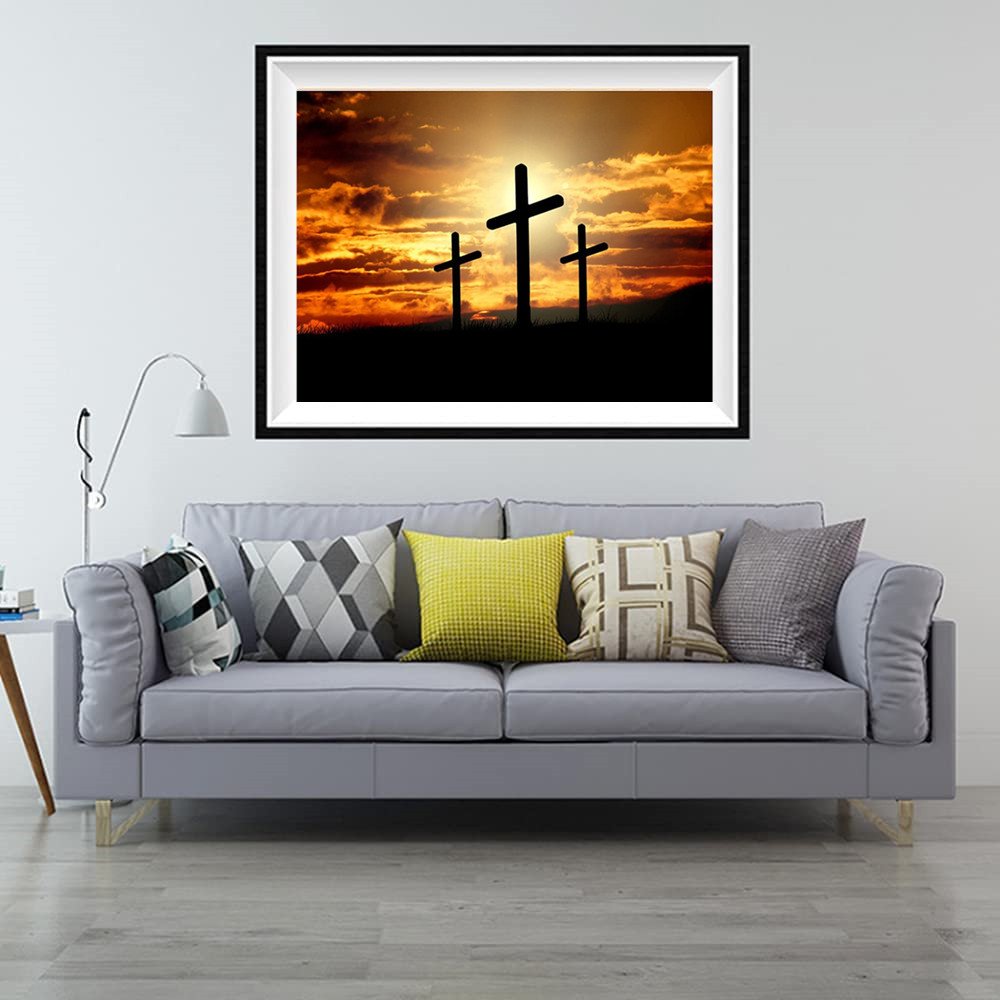 Framed artwork of three crosses silhouetted against a dramatic sunset sky, displayed above a gray sofa.