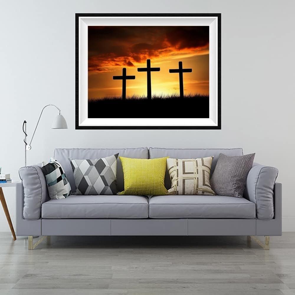 Framed diamond painting of three crosses silhouetted against a dramatic sunset sky, displayed above a gray sofa.