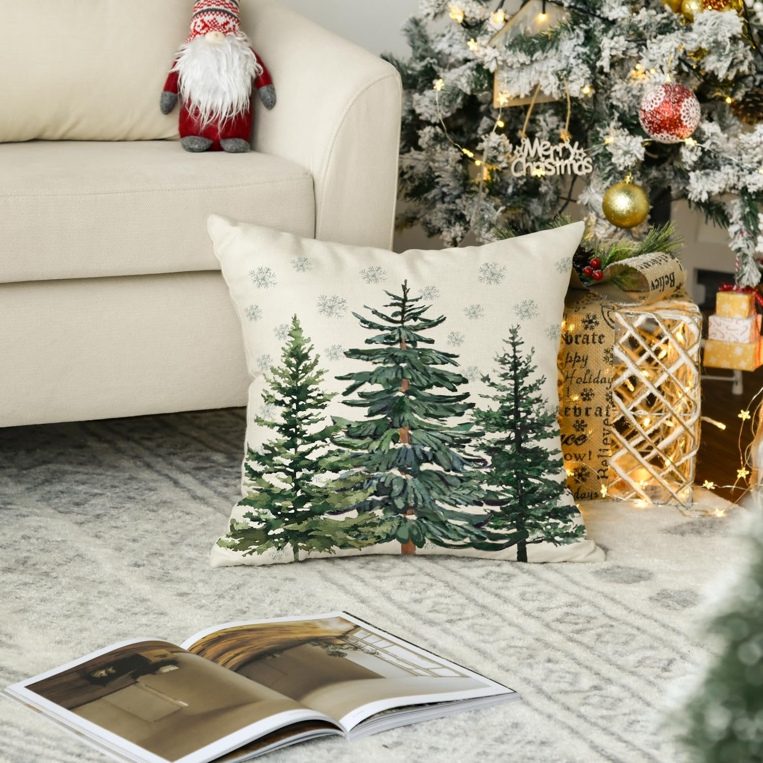 Christmas throw pillow cover with watercolor pine trees and snowflakes on a couch next to a decorated Christmas tree.