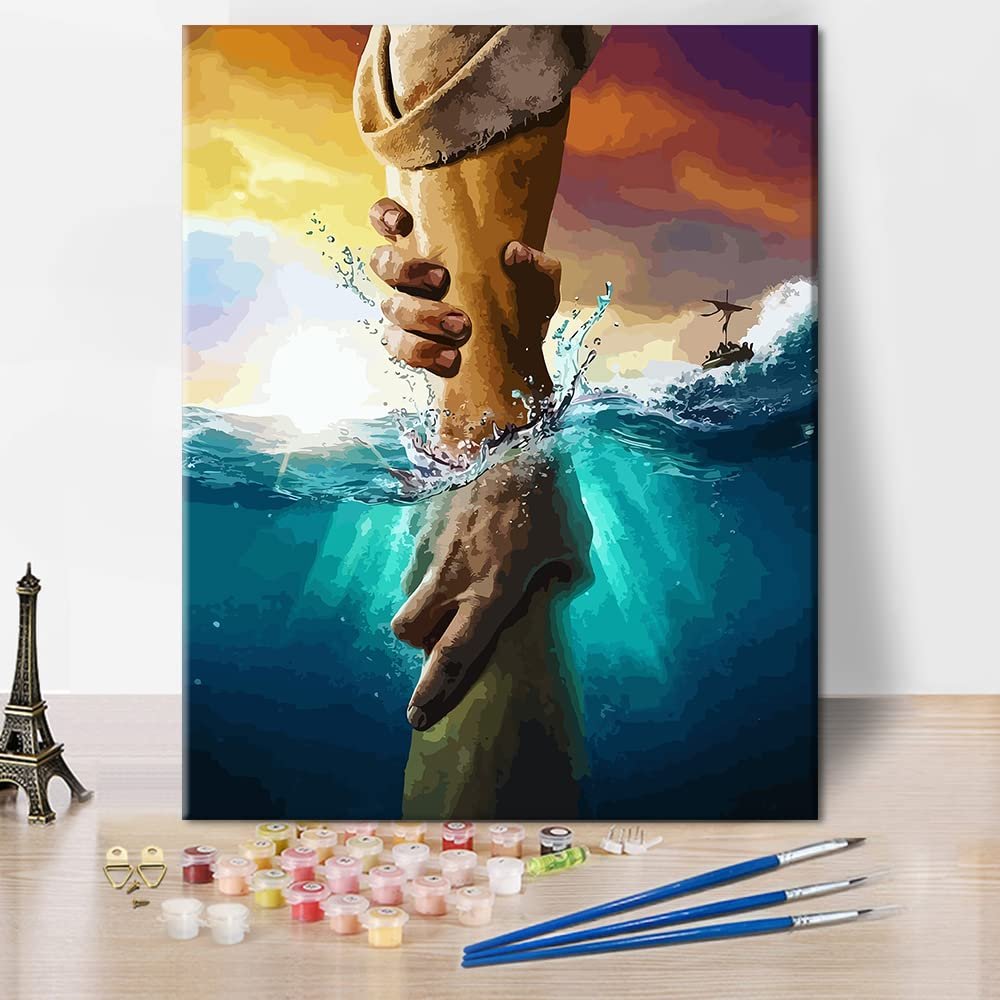 Paint by numbers kit showing Jesus reaching down to help someone out of the water, with paints and brushes in foreground.