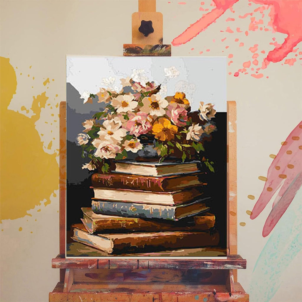 Paint by numbers canvas showing a stack of antique books with a floral arrangement on top, displayed on an easel.
