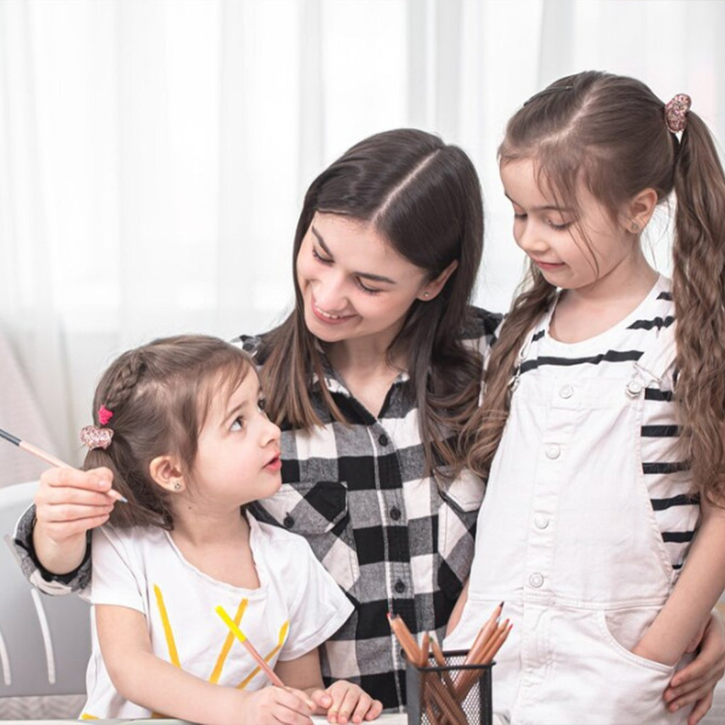 Woman and two young girls looking at a drawing surface with pencils and brushes