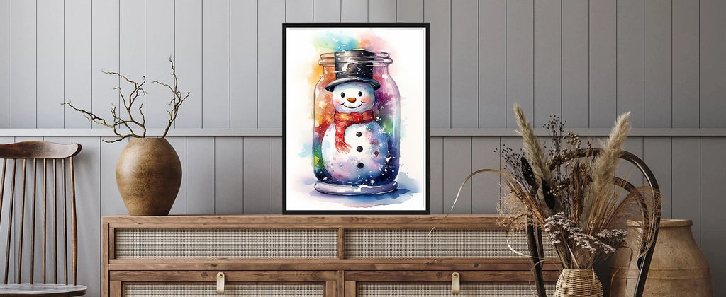 Framed watercolor painting of a snowman in a jar with a red scarf and black hat, displayed on a wooden dresser.
