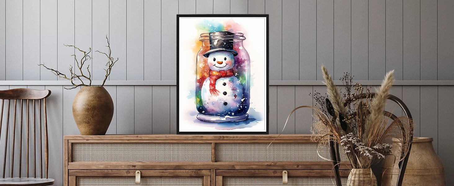 Framed watercolor painting of a snowman in a jar with a red scarf and black hat, displayed on a wooden dresser.