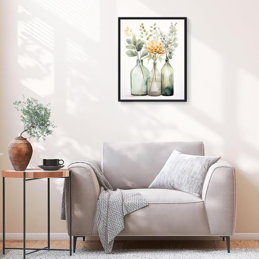 Framed watercolor painting of three glass bottles with yellow flower and green foliage, displayed above a sofa.