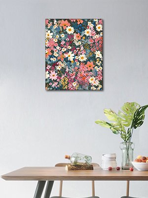 Frameless floral acrylic paint by number kit canvas hanging on a wall above a wooden table with a vase of plants.