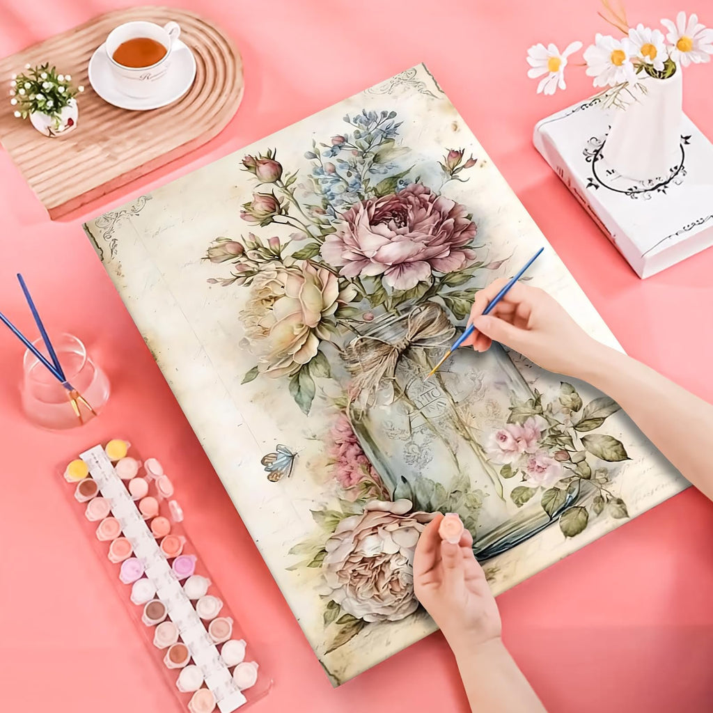 Hands painting a floral design on canvas with paint pots and brushes nearby