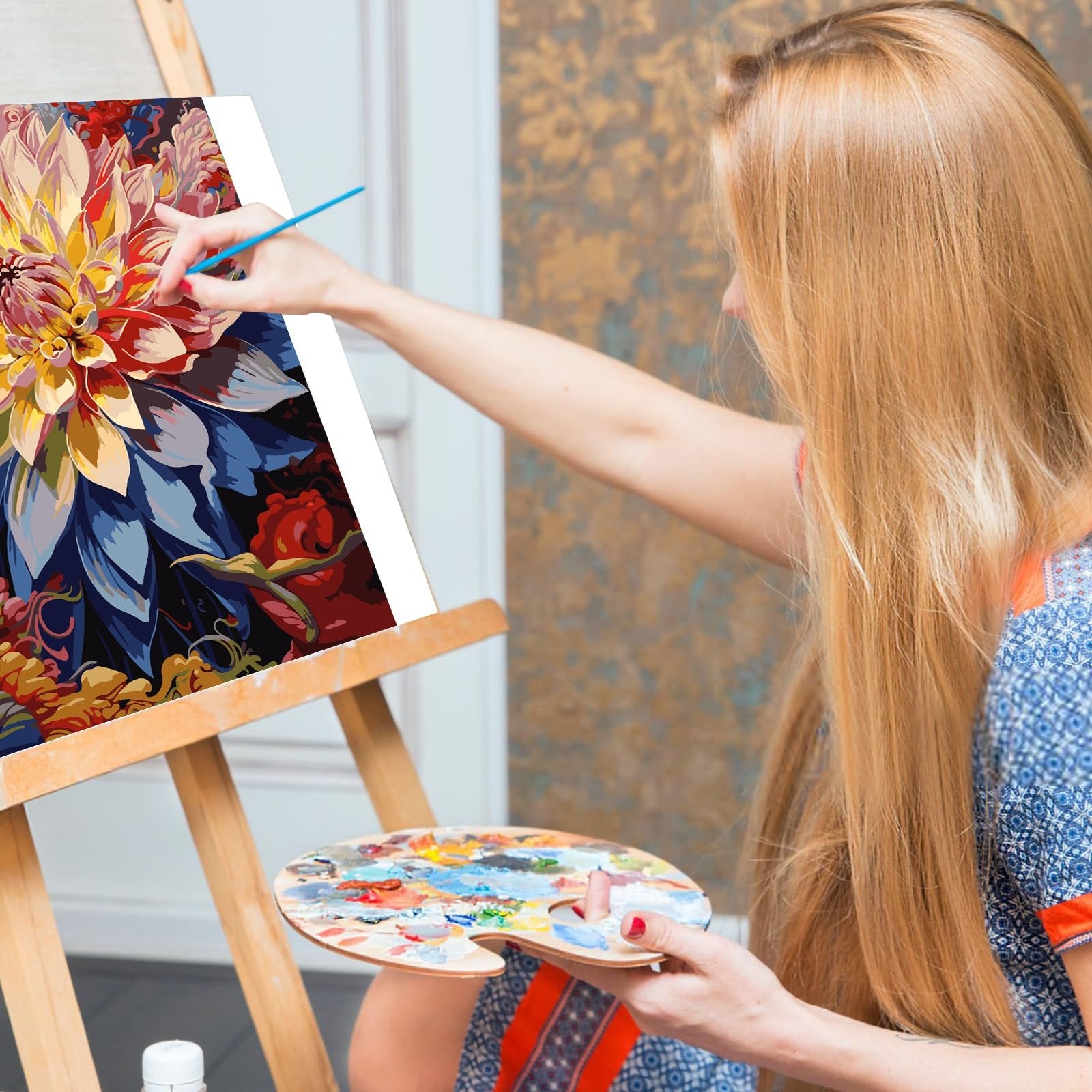 Woman painting a floral design on canvas using a paint-by-numbers kit, holding a palette.