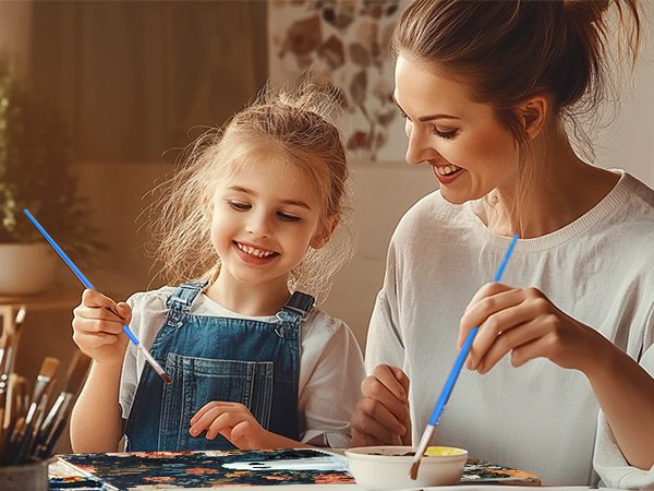 Mother and daughter painting a ghost-themed picture together, smiling and holding brushes.