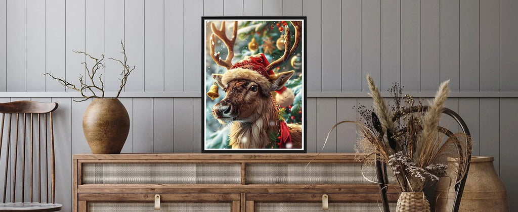 Framed Christmas reindeer painting with Santa hat and bell, displayed on a wooden dresser with decorative vases.