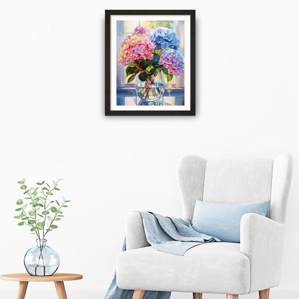 Framed painting of colorful hydrangeas in a glass vase on a table, displayed in a living room setting with an armchair.