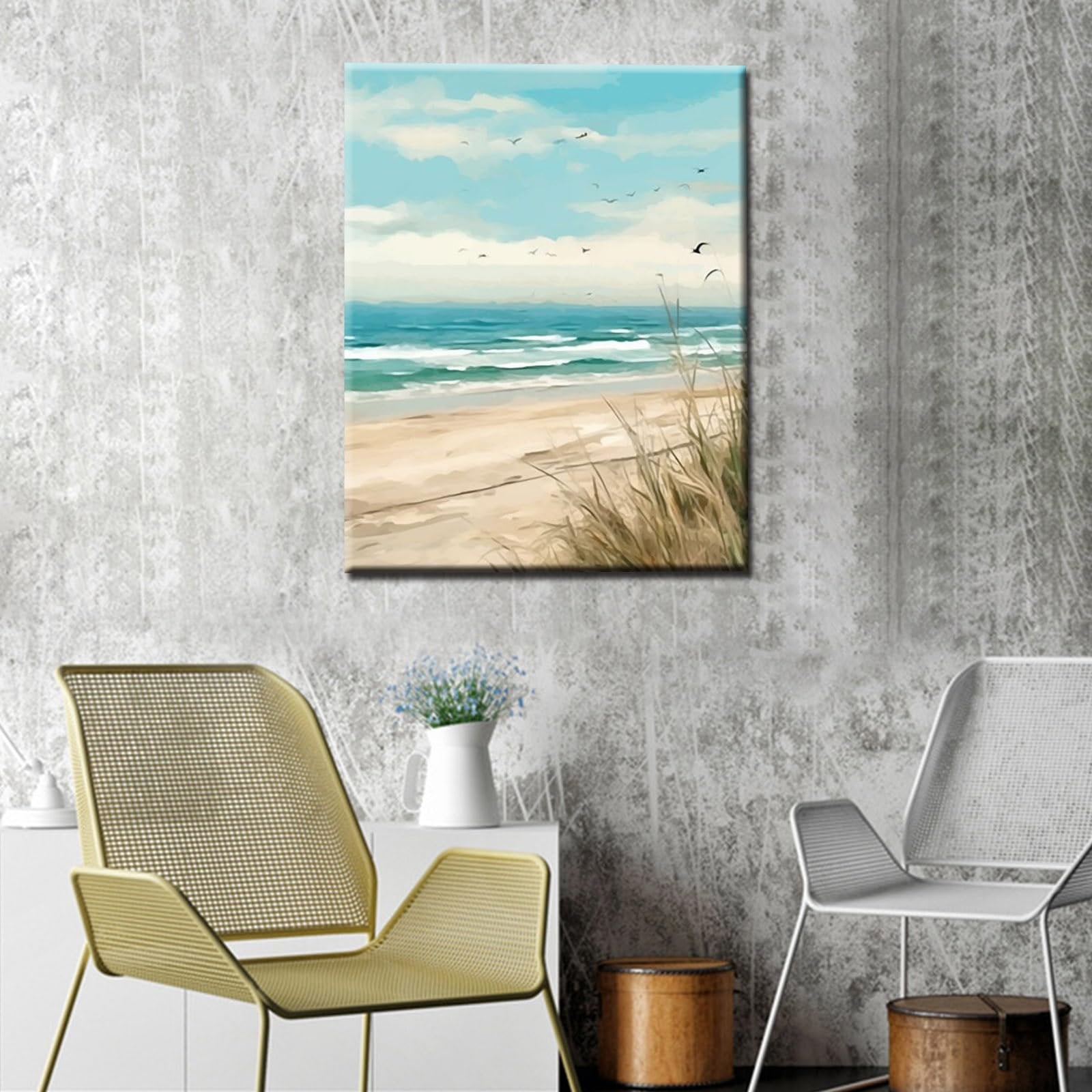 Canvas painting of a serene beach scene with waves, sand, and birds in the sky, displayed on a textured wall between two chairs.