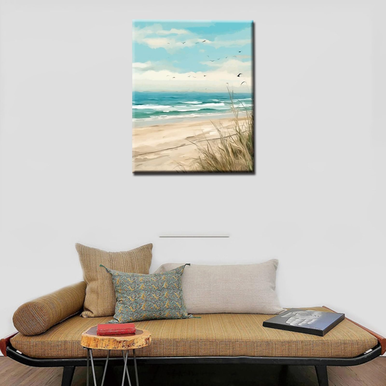Seaside beach painting with waves, sand, and seagulls in the sky, displayed on a wall above a couch.