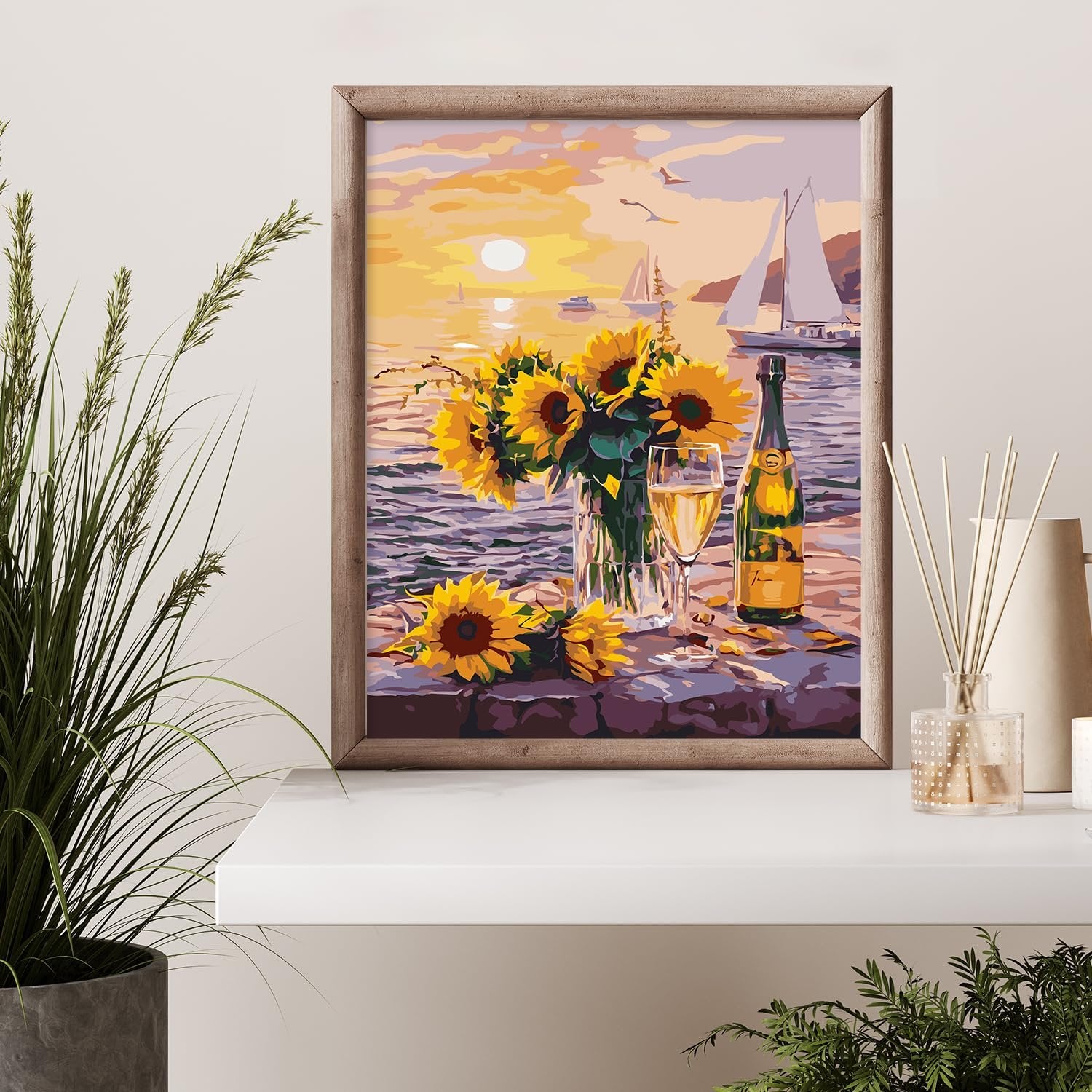 Paint by numbers kit artwork of sunflowers and champagne by the sea at sunset, framed.
