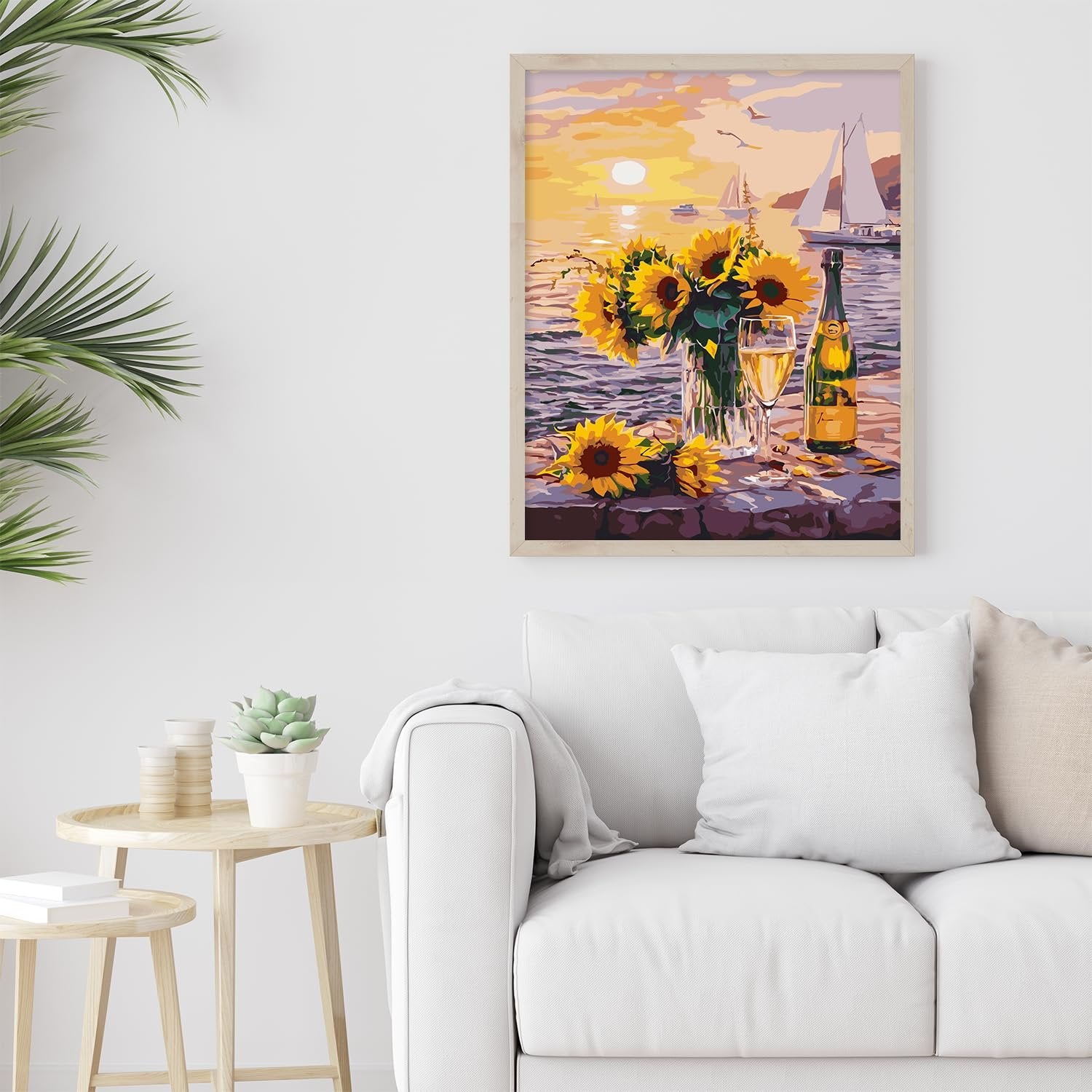 Paint by numbers artwork of sunflowers and champagne by the sea at sunset, framed and hanging above a sofa.