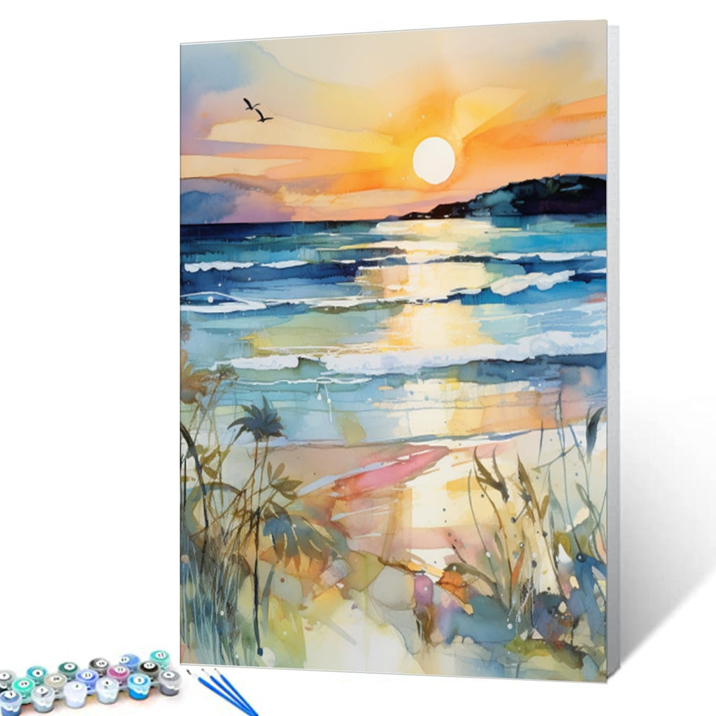 Paint by numbers kit showing a watercolor sunset beach scene with waves and reeds, with acrylic paint pots and brushes in foreground.