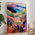 Framed colorful abstract mountain wildflower wall art poster leaning against a white wall with a plant and chair nearby.