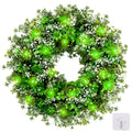 St. Patrick's Day shamrock wreath with green LED lights, plastic clover and flower accents, shown on a white background with a hook accessory.